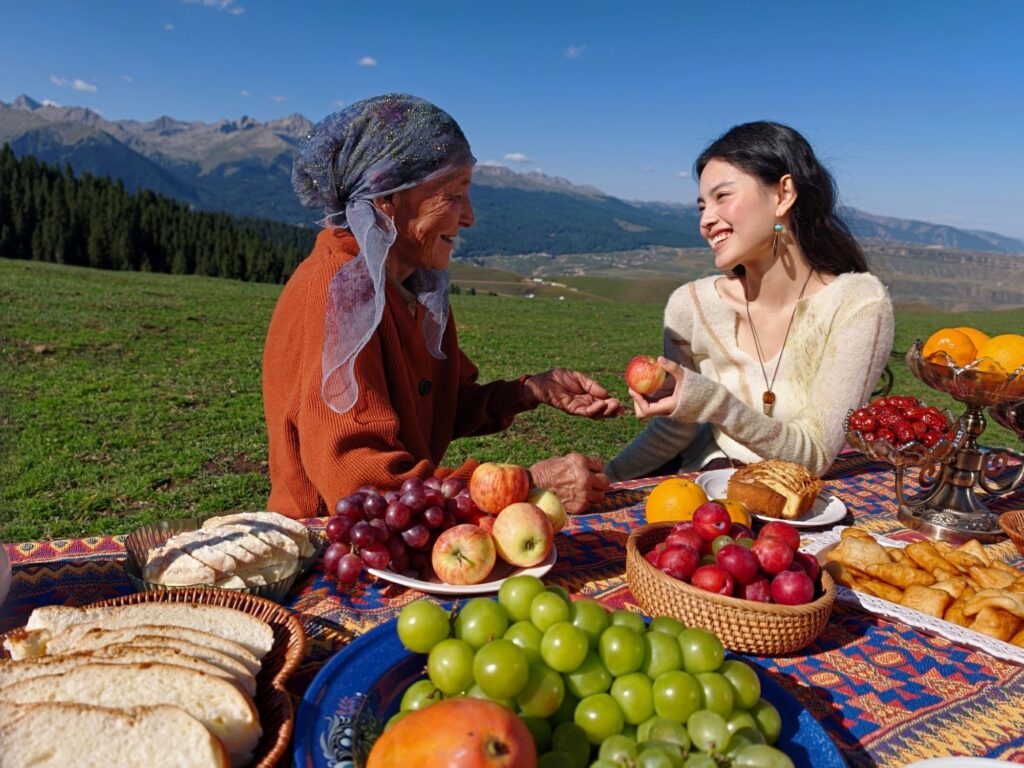 Two women sharing fruit at a picnic on a mountain meadow, shot on a smartphone main camera